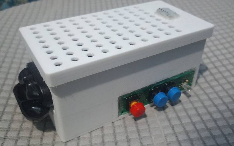 The EarPrompt device: a white 3D-printed enclosure with a perforated lid and a microphone module on top, a front panel with one red and two blue buttons and a status LED, and a Bluetooth earbud case docked on the side.